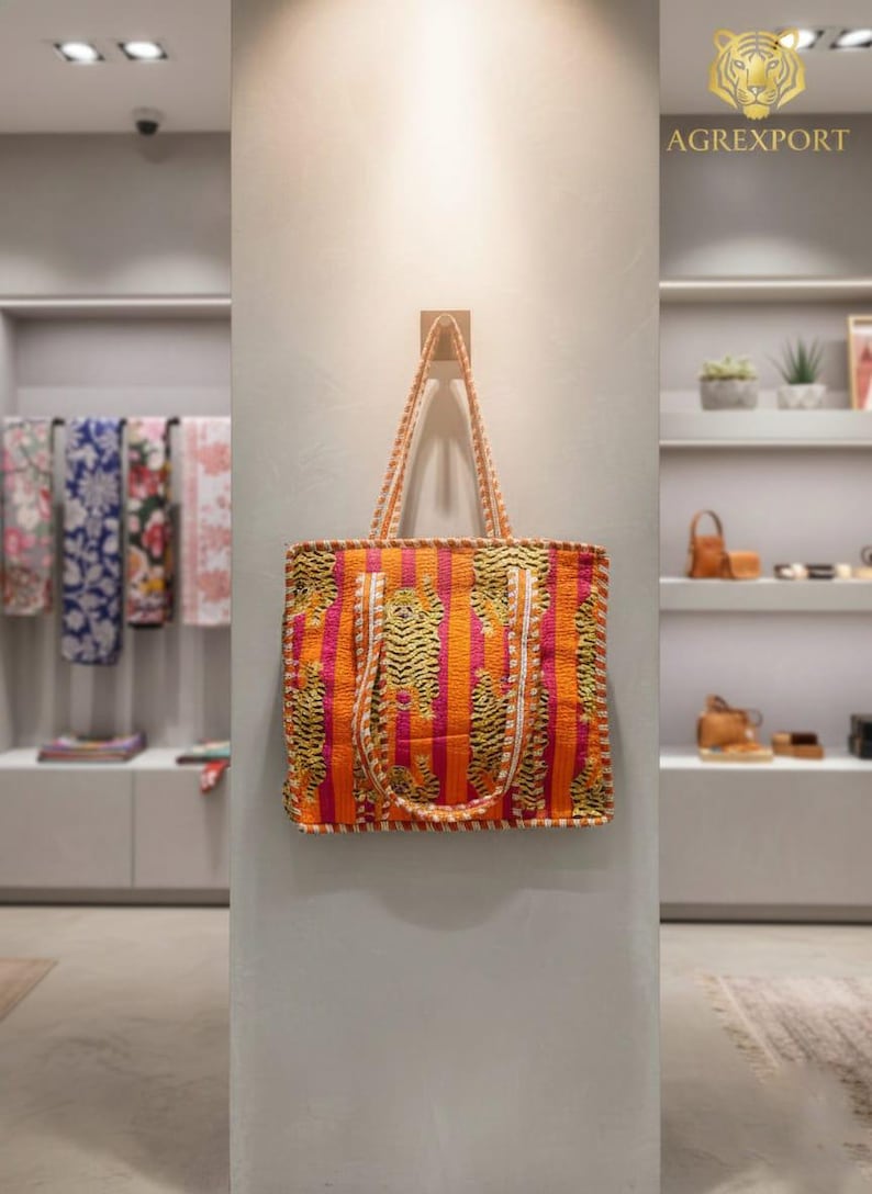 May include: An orange and pink tote bag with a striped pattern and tiger print accents. The bag has long handles and is hanging on a wall. The bag is part of a collection of bags and accessories.