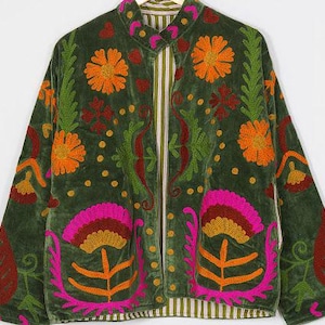 Op de afbeelding: Een olijfgroen fluwelen jasje met een opstaande kraag en lange mouwen. Het kledingstuk is versierd met levendig, meerkleurig bloemen- en bladerborduurwerk in tinten oranje, roze, rood en groen. De binnenvoering heeft een gestreept patroon.