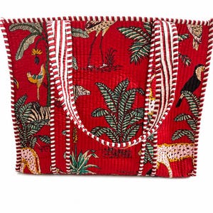May include: A red tote bag with a tropical jungle print featuring zebras, toucans, and palm trees. The bag has white and red striped handles and trim. The bag is quilted.