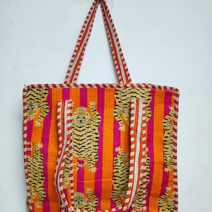 May include: A vibrant tote bag with a repeating tiger pattern on a striped orange and pink background. The bag has matching orange and white striped handles and trim. The bag is made of a quilted fabric.