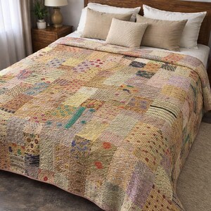 Puede incluir: Un edredón patchwork en tonos beige, amarillo y rosa, con varios cuadrados estampados. El edredón está sobre una cama con almohadas beige y un cabecero de madera. Sus dimensiones son de aproximadamente 203 cm por 229 cm.