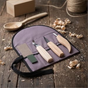 Puede incluir: Un juego de tallado de madera con tres cuchillos, una piedra de afilar y una funda de transporte morada. También hay una cuchara de madera, un bloque de madera y virutas de madera. Las herramientas tienen mangos de madera y hojas de metal.