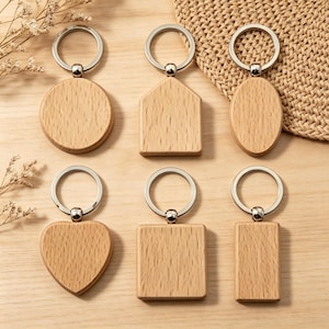 May include: Six wooden keyrings in different shapes: circular, house, oval, heart, square, and rectangular. Each keyring has a silver-coloured metal ring and a small, round connector. The keyrings are made of light-coloured wood.