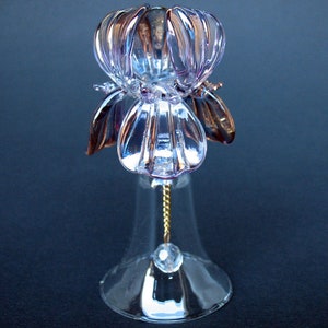 May include: A glass bell with a purple and clear glass flower design. The bell has a gold chain attached to the flower.