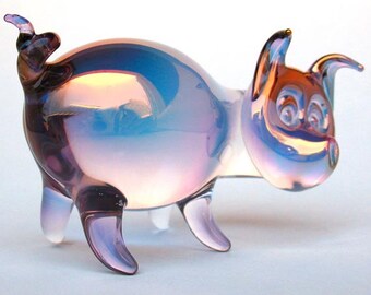 May include: A glass pig figurine with iridescent purple and blue coloring. The pig has a curled tail and a whimsical expression.