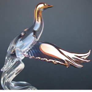 May include: A glass bird figurine with iridescent wings. The bird is in flight with its wings spread wide. The body of the bird is clear glass, while the wings have a pink and gold iridescent finish.