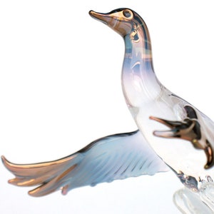May include: A glass sculpture of a bird in flight with iridescent blue and white wings and a gold beak. The bird is in mid-air with its wings spread wide.
