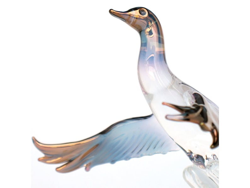 May include: A glass sculpture of a bird in flight with iridescent blue and white wings and a gold beak. The bird is in mid-air with its wings spread wide.