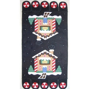 May include: A felt penny rug with a gingerbread house design. The rug is black with white snowflakes and two gingerbread houses with red and white candy cane trim. The rug is 24 inches by 12 inches.