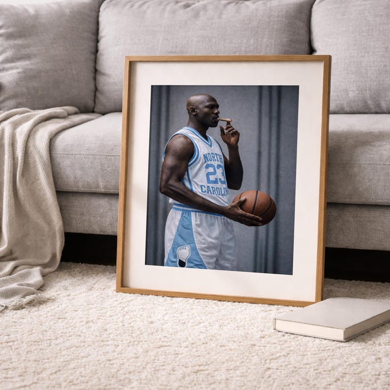 Puede incluir: Impresi&oacute;n enmarcada de un jugador de baloncesto con una camiseta azul claro y blanca con el n&uacute;mero 23. El jugador sostiene una pelota de baloncesto y un cigarro. La impresi&oacute;n est&aacute; en un marco de madera, sobre una alfombra blanca.
