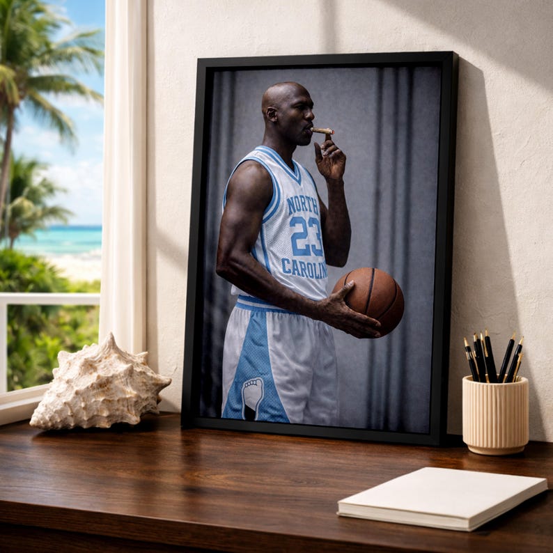 Puede incluir: Impresi&oacute;n enmarcada de un jugador de baloncesto con una camiseta azul claro y blanca con el n&uacute;mero 23. El jugador sostiene un bal&oacute;n de baloncesto y un cigarro. La impresi&oacute;n est&aacute; sobre una superficie de madera cerca de una ventana.