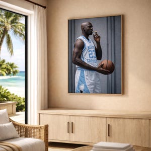 Puede incluir: Impresi&oacute;n enmarcada de un jugador de baloncesto con una camiseta azul claro y blanca con el n&uacute;mero 23. El jugador sostiene una pelota de baloncesto y un cigarro. La impresi&oacute;n se exhibe en una habitaci&oacute;n con vista al mar.