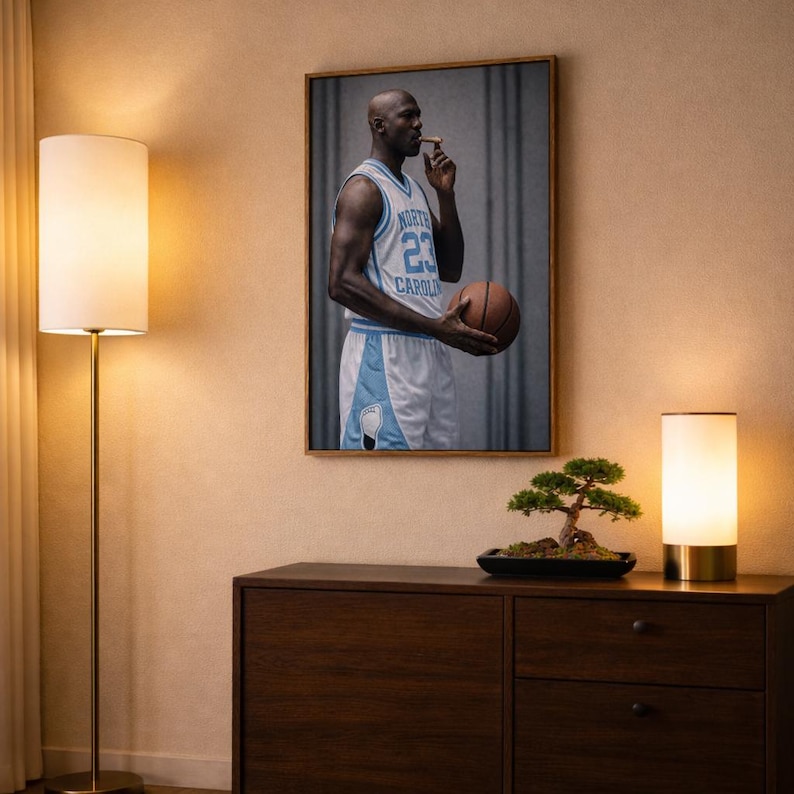 Puede incluir: Una impresi&oacute;n enmarcada de un jugador de baloncesto con una camiseta azul claro con el n&uacute;mero 23, sosteniendo una pelota de baloncesto y un cigarro. La impresi&oacute;n cuelga sobre un mueble de madera oscura, con un bons&aacute;i y una l&aacute;mpara.