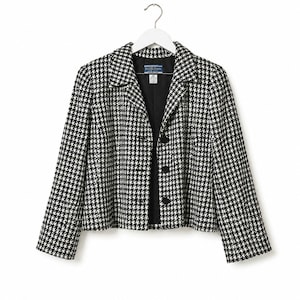 May include: A black and white houndstooth patterned blazer with a notched collar, long sleeves, and a three-button front closure. The jacket features a black interior lining and a Pendleton brand label at the inner neckline, hanging on a white hanger.