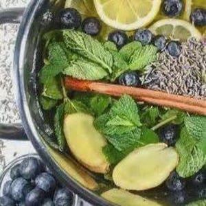 May include: A close-up of a stainless steel pot filled with ingredients for a beverage. The pot contains lemon slices, blueberries, mint leaves, ginger slices, and a cinnamon stick. Dried lavender and rice are also visible.