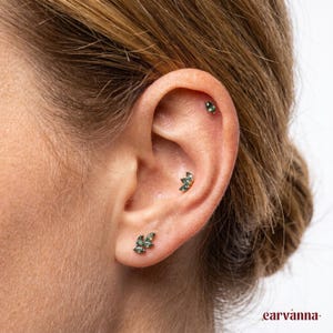 May include: Three gold-toned earrings featuring marquise-cut green gemstones. One single-stone stud is placed in the upper cartilage, a three-stone cluster in the conch, and a three-stone cluster in the earlobe, all set in a metallic gold finish.
