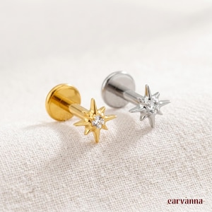 May include: Two flat back labret studs featuring a starburst design. One stud is gold-toned with a central clear stone, and the other is silver-toned with a central clear stone. Both pieces have a flat circular base and a post for secure fastening.