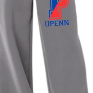 May include: Grey wide-leg sweatpants featuring a white drawstring and the word "UPENN" in blue and red block letters. The trousers appear to be made of a soft material.
