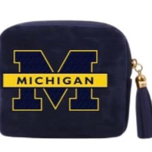 Può includere: Un piccolo astuccio quadrato blu navy con cerniera e nappa dorate. La parte anteriore presenta un grande logo "MICHIGAN" giallo e blu navy. L'astuccio è probabilmente realizzato in un materiale morbido e strutturato.