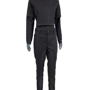 May include: Black two-piece outfit. The top is a cropped jacket with a high collar and long sleeves. The trousers are high-waisted with a button closure and a tailored fit. White stitching details the seams of the jacket and trousers.