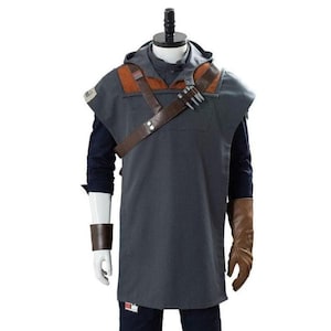 May include: A grey hooded tunic with brown leather details and a shoulder strap, part of a costume. The costume includes a dark blue long-sleeved shirt, brown gloves, and a wrist cuff. The outfit is displayed on a mannequin.