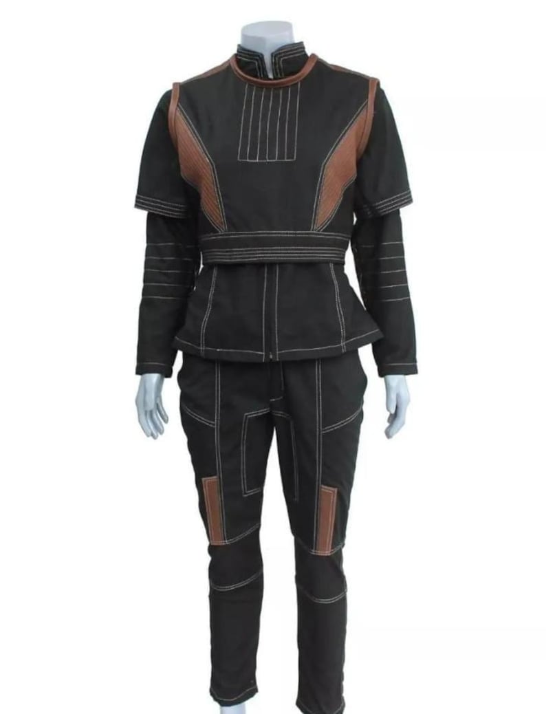 Puede incluir: Traje negro con detalles marrones y costuras blancas. El conjunto incluye una chaqueta con cuello alto y un pantal&oacute;n a juego. La chaqueta tiene un dise&ntilde;o &uacute;nico con paneles marrones en los hombros y el pecho. Los pantalones tienen parches marrones en las rodillas.