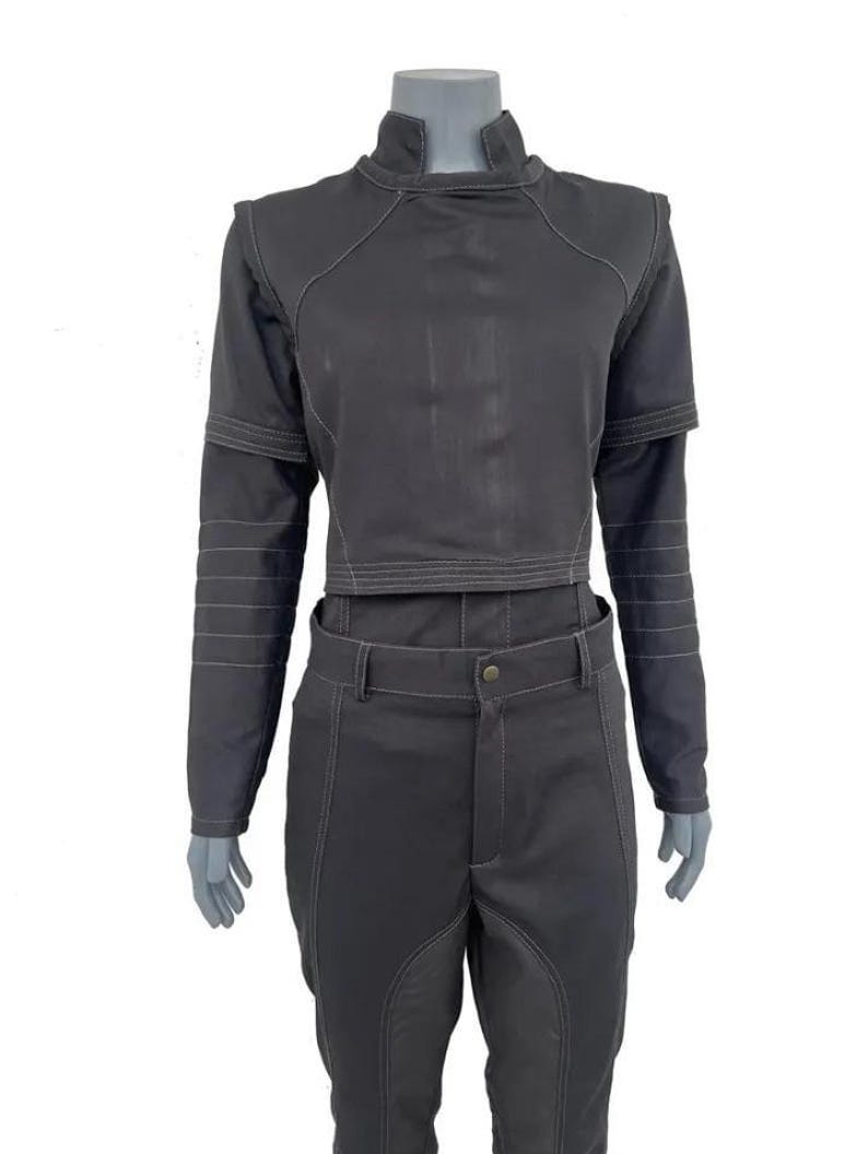May include: A dark grey two-piece outfit. The cropped top has a high collar and long sleeves, and the matching trousers have a button closure. White stitching details are visible throughout the outfit, with horizontal stitching on the sleeves.