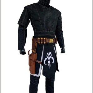 Puede incluir: Traje negro con costuras blancas, con cuello alto y mangas cortas. El atuendo incluye un cintur&oacute;n marr&oacute;n con porta balas, una funda y una falda negra con un emblema blanco. Un disfraz de cosplay.