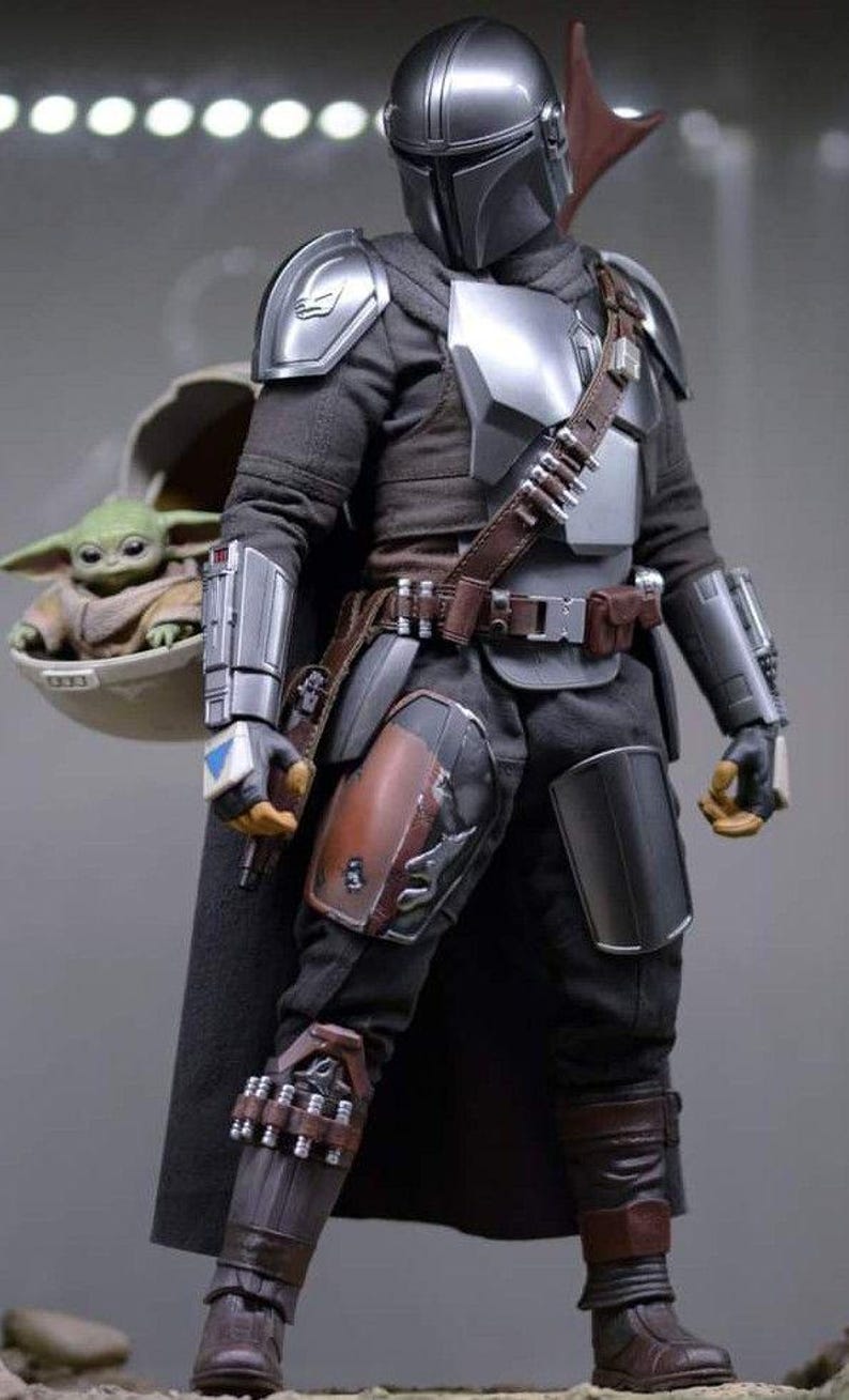 Puede incluir: Figura de acci&oacute;n detallada de The Mandalorian con armadura plateada y negra, con cintur&oacute;n y capa de cuero marr&oacute;n. La figura lleva un peque&ntilde;o alien&iacute;gena verde en una c&aacute;psula flotante. La figura est&aacute; en una pose din&aacute;mica.