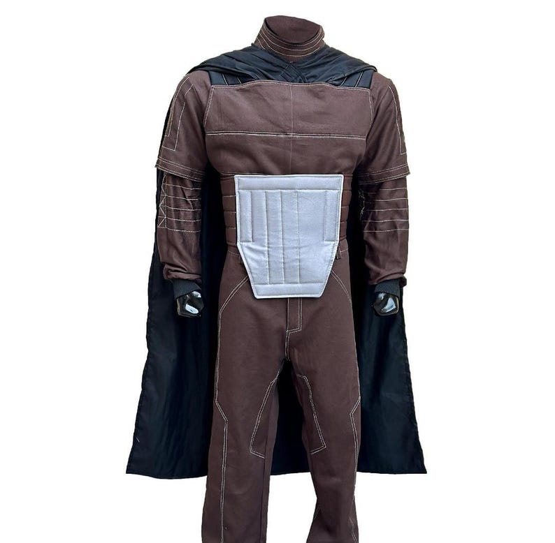 Puede incluir: Un disfraz marr&oacute;n con una capa negra. El disfraz tiene un cuello alto, mangas largas y costuras blancas. Un panel gris plateado est&aacute; en el pecho. El disfraz est&aacute; dise&ntilde;ado para parecerse a un personaje de una pel&iacute;cula de ciencia ficci&oacute;n.