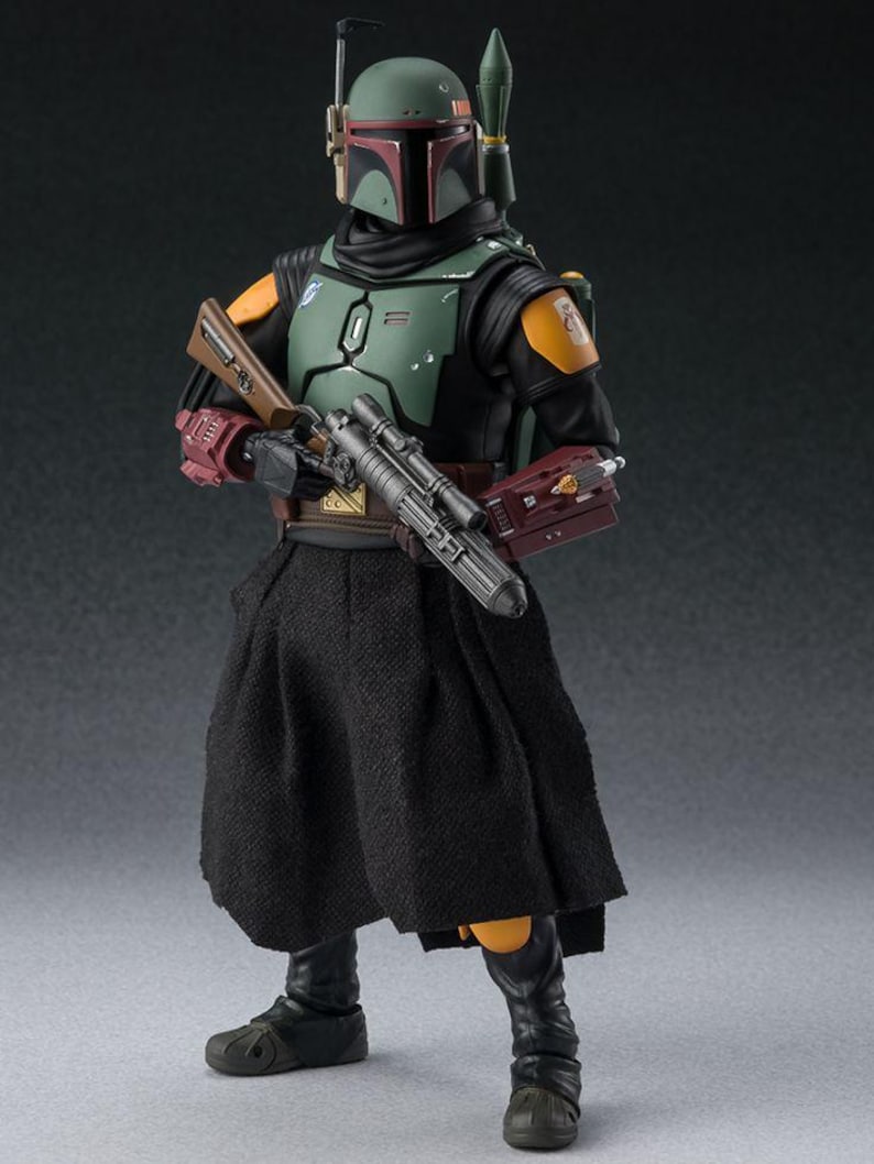May include: A detailed action figure of Boba Fett from Star Wars. The figure is clad in a green, black, and orange armored suit, complete with a helmet and jetpack. It holds a blaster rifle and wears a black skirt-like garment. The figure stands on a neutral background.