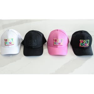 Puede incluir: Cuatro gorras de béisbol en blanco, negro y rosa. Cada gorra tiene el texto "VOLT PUNK" en un diseño rectangular colorido en la parte delantera. Las gorras están dispuestas en una fila, mostrando la variedad de colores y diseños.