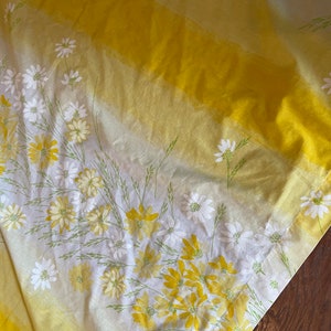 May include: Yellow and white striped fabric with a floral pattern of white daisies and yellow flowers. The fabric has a gradient effect, fading from a darker yellow to a lighter yellow.