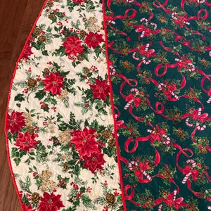 May include: A reversible Christmas tree skirt with a white background featuring red poinsettia flowers and a green background with red ribbons and candy canes.