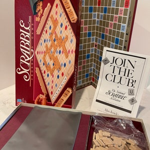 May include: A red and black box containing a Scrabble board game. The box includes a game board, letter tiles, and instructions. The box also includes a flyer that says "Join the Club! The National Scrabble Association".