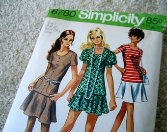 May include: Simplicity sewing pattern number 8780 for a junior size 7 dress with a bust of 31 inches and a waist of 22 1/2 inches. The pattern shows three different styles of dresses, one in brown with a white belt, one in green with a white pearl necklace, and one in red and white stripes with a white skirt.