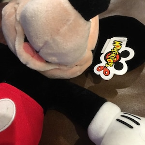 May include: A black and red plush Mickey Mouse toy with a white tag that says "Mouseketoys".