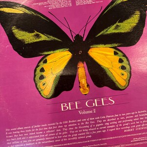 May include: Vintage vinyl record album cover featuring a large butterfly illustration in black, yellow, and green on a purple background. The album title "BEE GEES Volume 2" is displayed prominently. The cover has text describing the album.