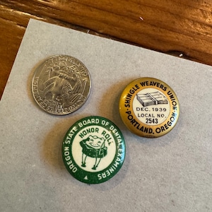 May include: Three vintage pinback buttons and a quarter. One button is gold with text "Shingle Weavers Union" and "Dec. 1939". Another is green and white with a frog graphic and text "Oregon State Board of Dental Examiners".