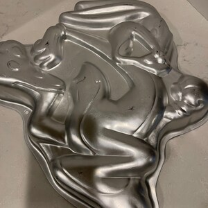 May include: A silver metal cake pan shaped like Bugs Bunny. The pan is designed to create a three-dimensional cake of Bugs Bunny.