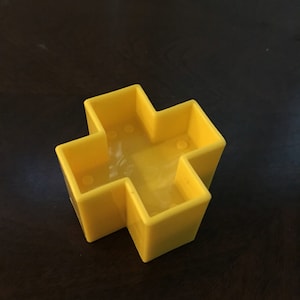 May include: A yellow plastic cross-shaped toy with four open compartments.