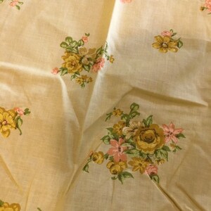 May include: A beige fabric with a floral pattern featuring yellow and pink flowers. The fabric has a subtle texture and a soft, light feel.