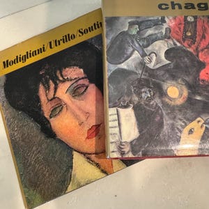 May include: Two vintage art books, one with a portrait of a woman with dark hair and red lips, titled "Modigliani/Utrillo/Soutine", and the other with a colorful abstract painting and the title "Chagall" on the cover.