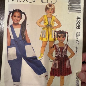 May include: McCall's sewing pattern featuring illustrations of children's clothing designs. The designs include overalls, a striped romper, and a polka-dot dress. The pattern number is 4326.