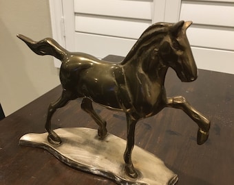 May include: A gold-toned metal horse sculpture standing on a wooden base. The horse is in a running pose with its head turned to the side.
