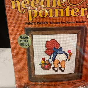 May include: Needlepoint kit featuring a girl in a red dress and blue overalls holding a basket of flowers. The kit includes 100% cotton canvas, 100% wool yarn, needle, mounting board, full color print and complete instructions. "Fancy Pants" design by Donna Kooler. Frame offer inside.