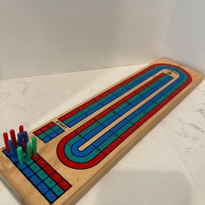 May include: A wooden cribbage board with a red, blue, and green track. The board has a "START" label and a row of pegs in red, blue, and green.