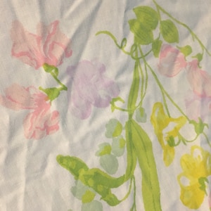 May include: A white fabric with a floral pattern featuring pink, purple, and yellow flowers with green leaves and stems.