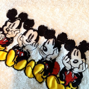 Puede incluir: Cuatro personajes de Mickey Mouse bordados con contornos negros, caras blancas y zapatos amarillos. Los personajes llevan todos pantalones cortos rojos y se tapan la cara con las manos.