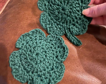 May include: Two crocheted green four-leaf clovers. The clovers are made with a green yarn and have a textured, bumpy surface.